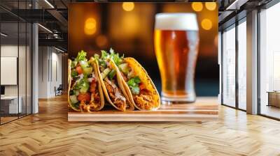 Three delicious tacos and a pint of beer served on a wooden table in a cozy restaurant with a blurred background of warm lights. Wall mural