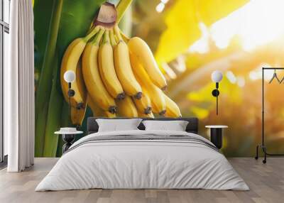 A bunch of ripe bananas hanging from a green leaf, illuminated by soft sunlight, showcasing their vibrant yellow color in a tropical setting. Wall mural