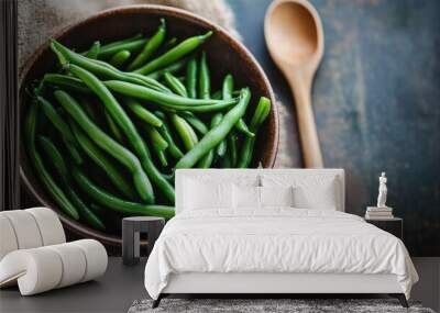 A bowl filled with fresh green beans and a rustic wooden spoon, with a focus on the vibrant color and texture of the beans against a simple, natural background. Wall mural