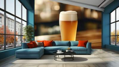 A frosty glass of beer with a thick, creamy foam head, set on a wooden table with a cozy pub background, highlighting its refreshing appeal. Wall mural