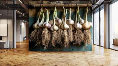 A high-resolution image of garlic bulbs hanging in a bunch, with their roots and stems still attached, drying in a rustic kitchen or storage area. Wall mural