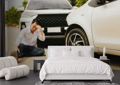 Asian man sits injured in front of his car after seeing the front of the car and damaging the bumper awaiting the insurance company and providing first aid : Accident and car insurance concept. Wall mural