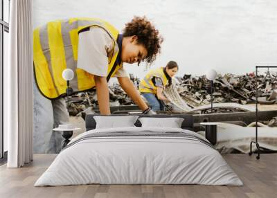 Two female workers working in an outdoor warehouse factory collecting old broken parts of old car parts are working together to sort broken parts in a pickup truck to keep order. Wall mural