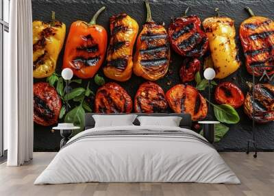 Top view of a variety of grilled paprikas with char marks, arranged on a black slate serving board. Wall mural