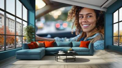 A happy smiling young woman drives a stylish car on vacation, emphasizing her relaxed posture and casual outfit. Wall mural