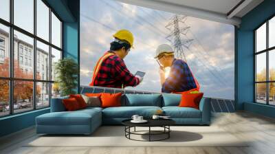 A team of two male electrical engineers using tablets to watch power stations and solar photovoltaic renewable energy panels. To plan the production of electricity at high voltage poles Wall mural