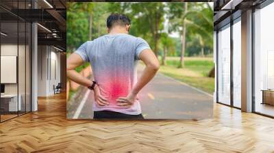 Young Asian men exercising in the park Pain in the back and using a hand to hold on my back That hurts while experiencing severe pain: exercise injury concepts Wall mural