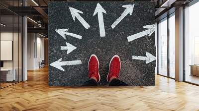 Person in red sneakers standing on an asphalt road surrounded by white arrows pointing in different directions, symbolizing open spaces and possibilities for future paths in a casual setting. Wall mural