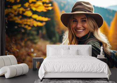 Joyful blonde woman in a hat exploring vibrant autumn forest trails with a smile Wall mural