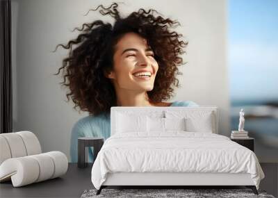 Joyful portrait of a young African American woman smiling confidently, gently touching her curly hair, radiating happiness in casual attire against a neutral background. Wall mural