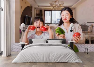 Young mother and daughter with vegetables at the table Wall mural