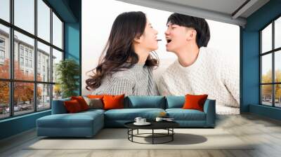 In winter, a pair of happy young Asian lovers sit on the sofa, mouth to mouth with each other, eating chocolate intimately

 Wall mural