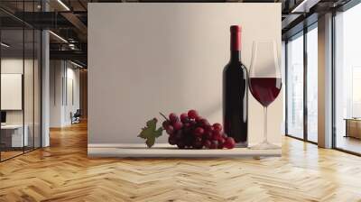 A bottle of red wine, a glass of red wine and a bunch of grapes on a white tabletop Wall mural