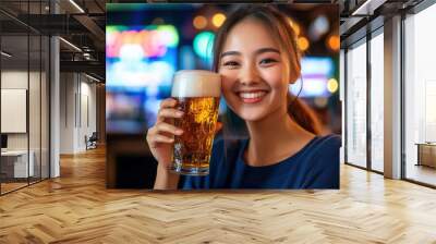 Young Asian woman with high ponytail, dressed in dark blue, sipping beer and smiling at the camera in a vibrant bar environment with a blurred nightclub background and copy space on the right. Wall mural