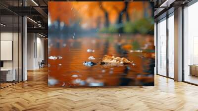 Serene river close-up with floating leaves and gentle rain amidst a backdrop of blurred trees adorned in vibrant orange foliage Wall mural