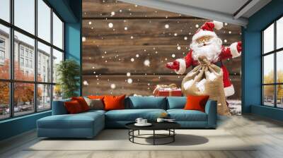 Santa Claus Toy with Bag of Gifts on Wooden Background with Snow - a festive and charming visual. The santa claus toy on the wooden background with snow and a bag of gifts creates an enchanting and de Wall mural