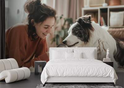 Beautiful woman with long hair holding smart phone while looking at dog in living room Wall mural