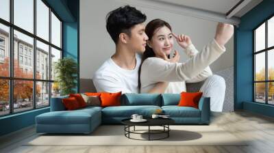 A young Asian couple taking pictures of each other on the sofa Wall mural