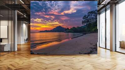 A breathtakingly beautiful sunset seaside scenery. The sky is ablaze with warm hues of orange, pink, and purple as the sun dips below the horizon. The waves gently lap at the shore, creating a soothin Wall mural