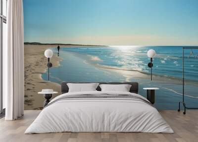 There is a person walking on a peaceful beach. The blue sea water is sparkling and the sky is soft. Wall mural