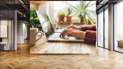 A closeup of hands typing on an open laptop, with coffee and digital tablet beside it on the wooden desk in front of bright window light Wall mural