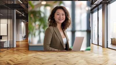 A photo of an attractive asian woman standing in the middle, smiling and holding her laptop computer while dressed for work in business casual attire with shoulder length curly hair Wall mural