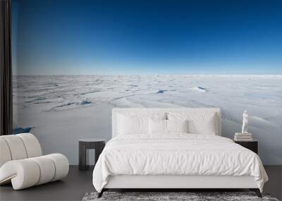 A vast expanse of white snow under the clear blue sky, creating an endless horizon Wall mural