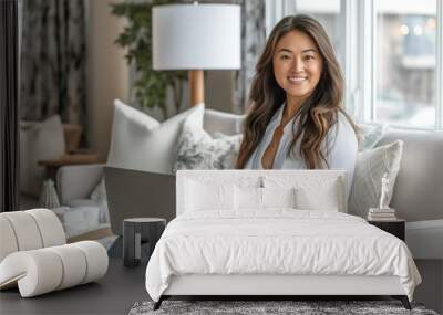 A woman in casual business attire sitting on the sofa of her modern apartment, working from home on her laptop and smiling at the camera Wall mural